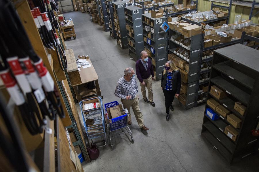 People walk through a warehouse with stacked boxes.