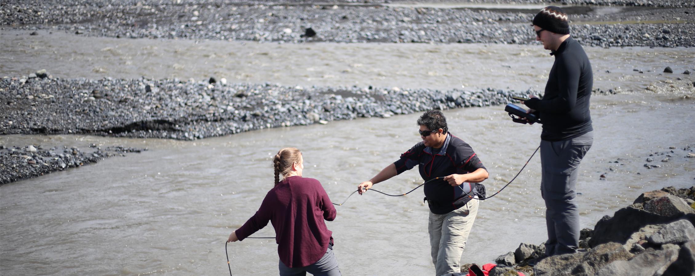 Three people work together and use technology to test a body of water.